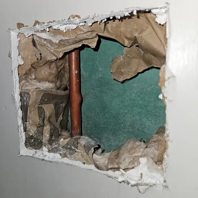 Drywall cut open to reach a leaking copper water pipe inside the wall