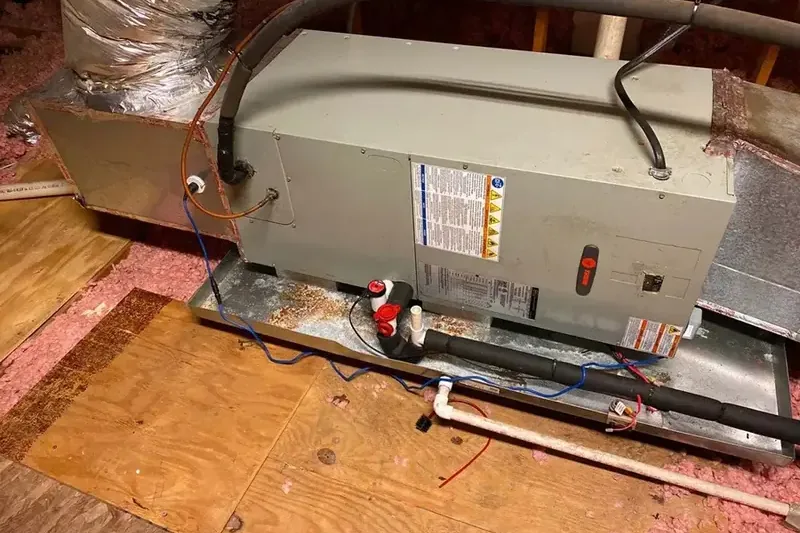 Attic air handler resting in its drain pan on plywood above the insulation