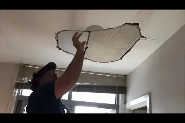 Worker pulling down a sagging, water-soaked section of ceiling below a roof leak